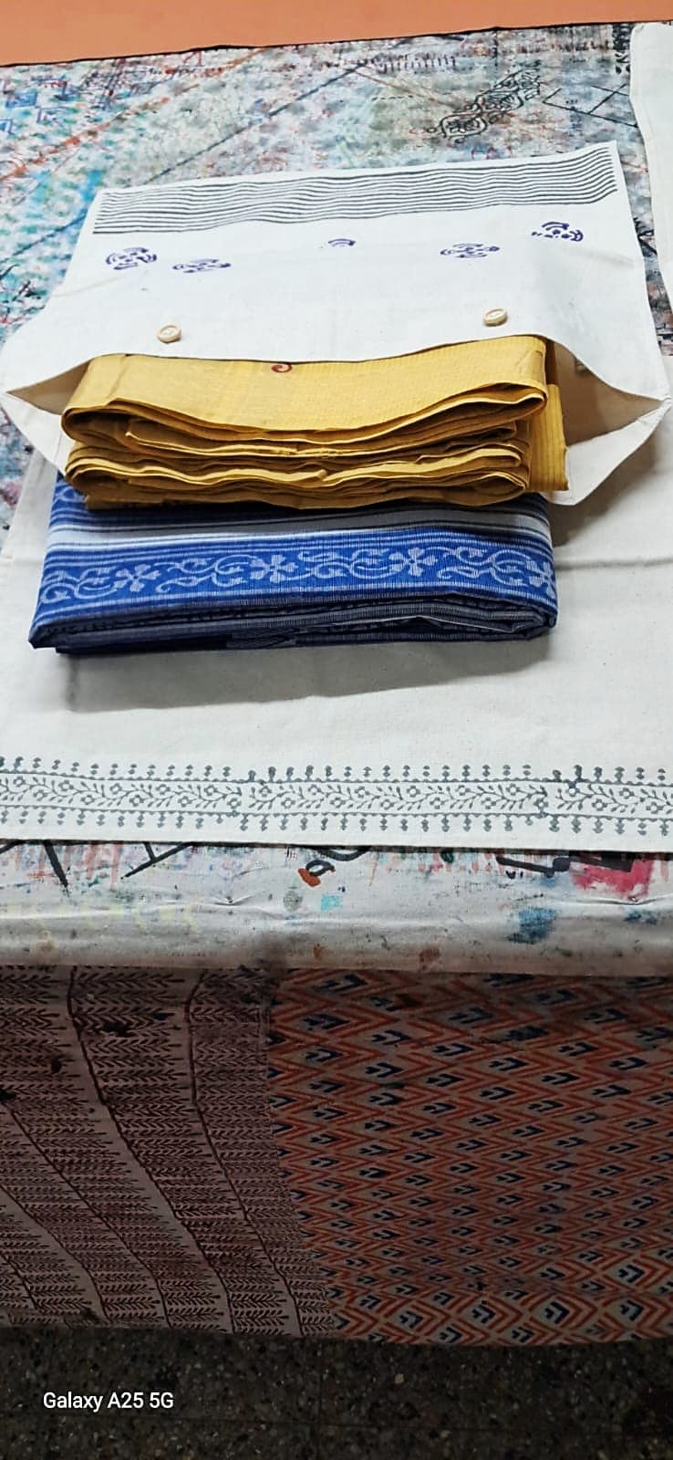 Block-printed white saree storage bag with wooden buttons, holding folded mustard and indigo sarees