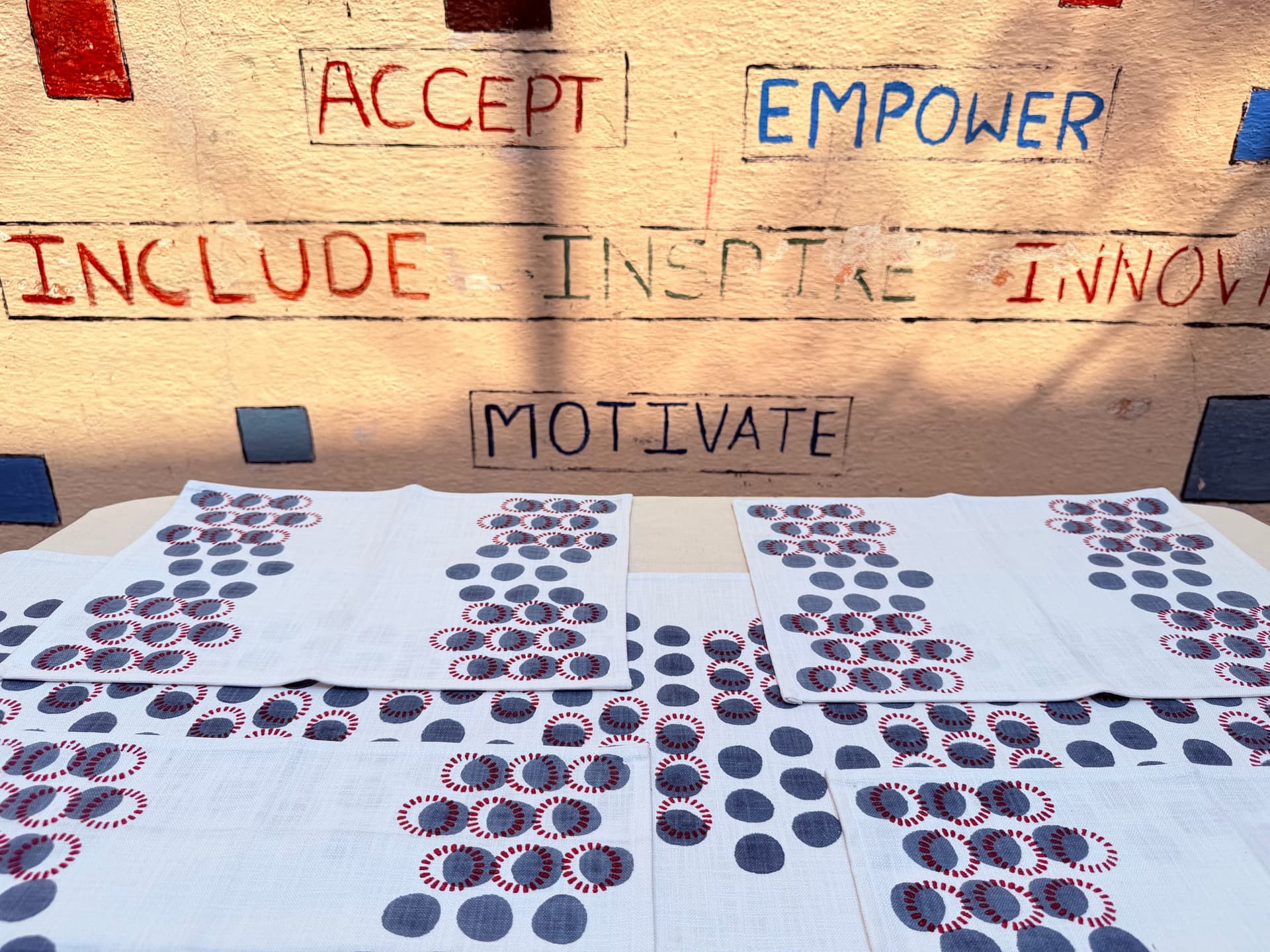 Freshly printed placemats dry beneath the studio wall painted with the words accept, empower, include, inspire, motivate
