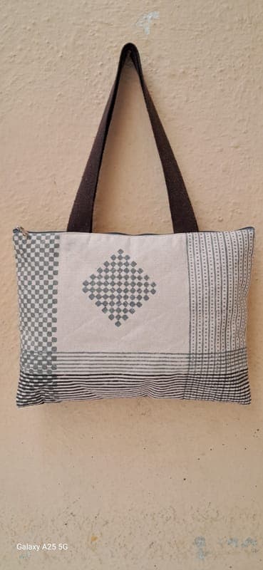 Quilted zip tote in grey and cream with a large cross-stitch diamond motif and checked block-printed borders, hanging on a cream wall
