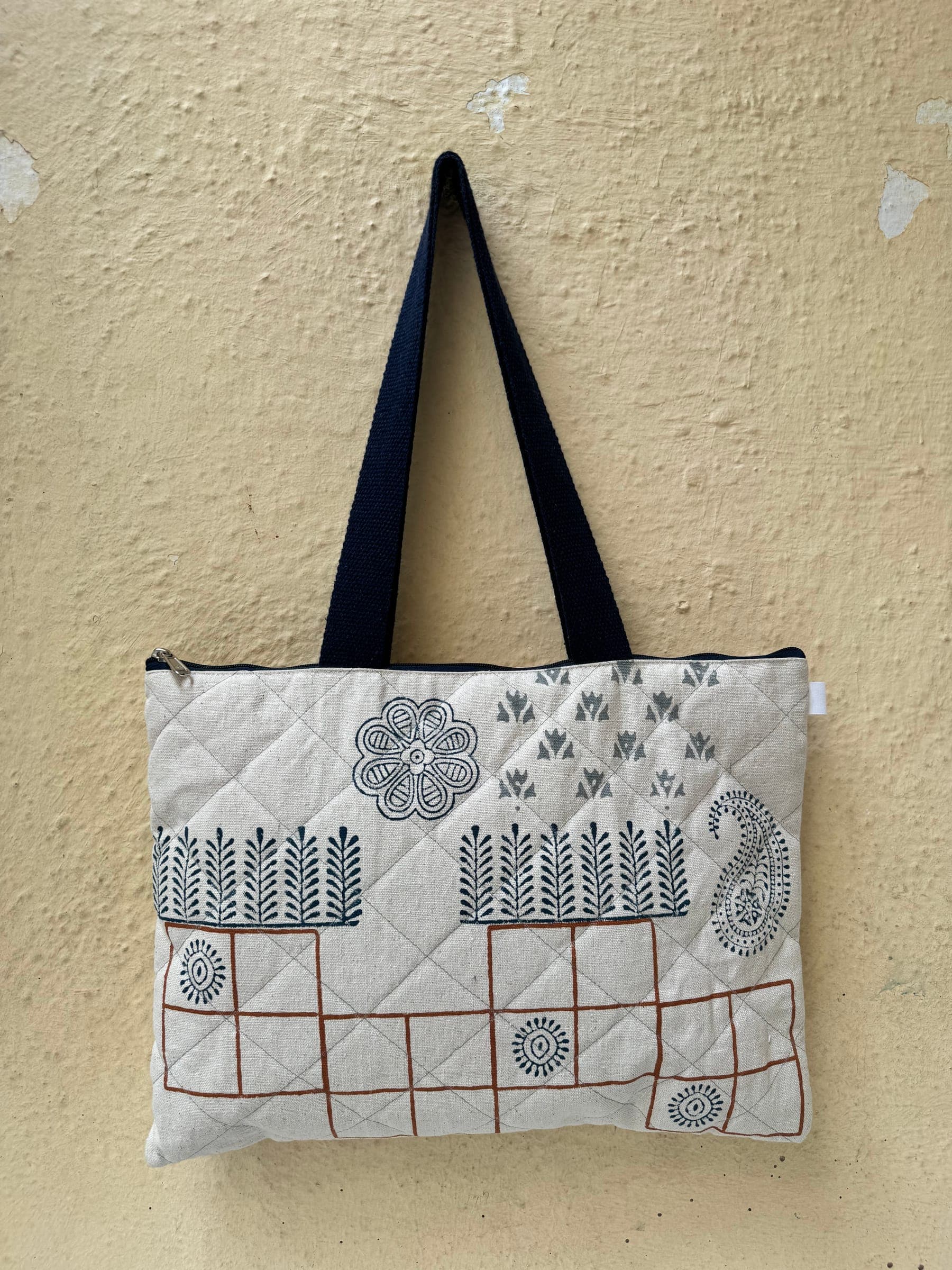 Quilted zip tote with hand-printed ferns, blossoms, paisley and a rust grid on cream, navy handles