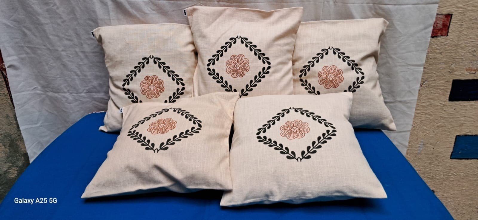 Five cream cushion covers with hand cross-stitched diamond medallions in rust and green