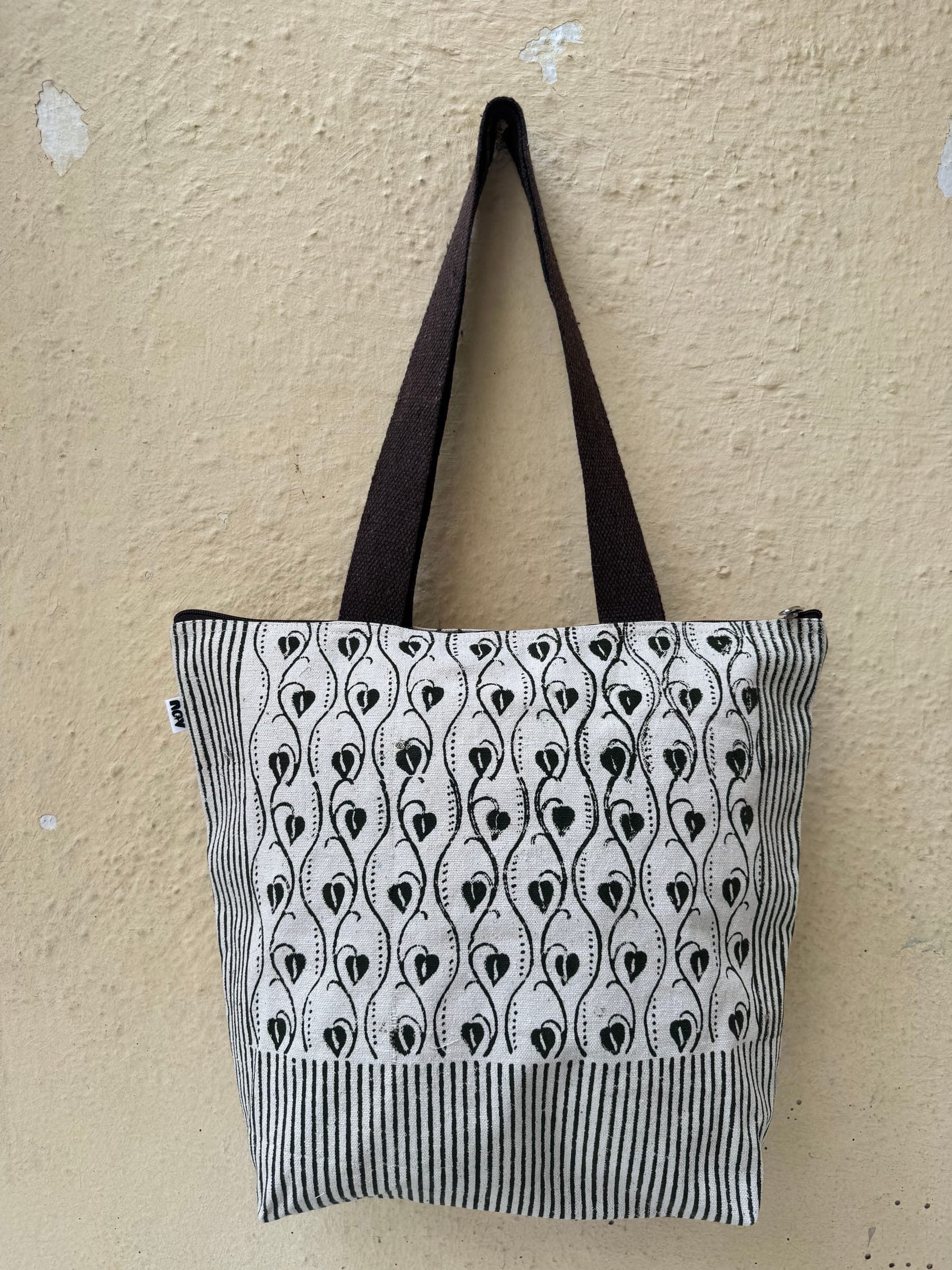 Cotton tote in a black and white peacock-feather drop print over a striped base, brown handles