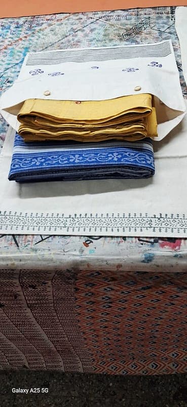 Block-printed white saree storage bag with wooden buttons, holding folded mustard and indigo sarees