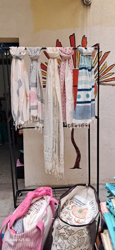 Block-printed cotton stoles in soft colours hanging from a display rack at the studio
