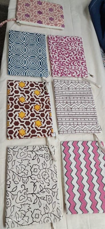Seven block-printed zip pouches laid out on a table, in magenta, mustard, plum and monochrome prints